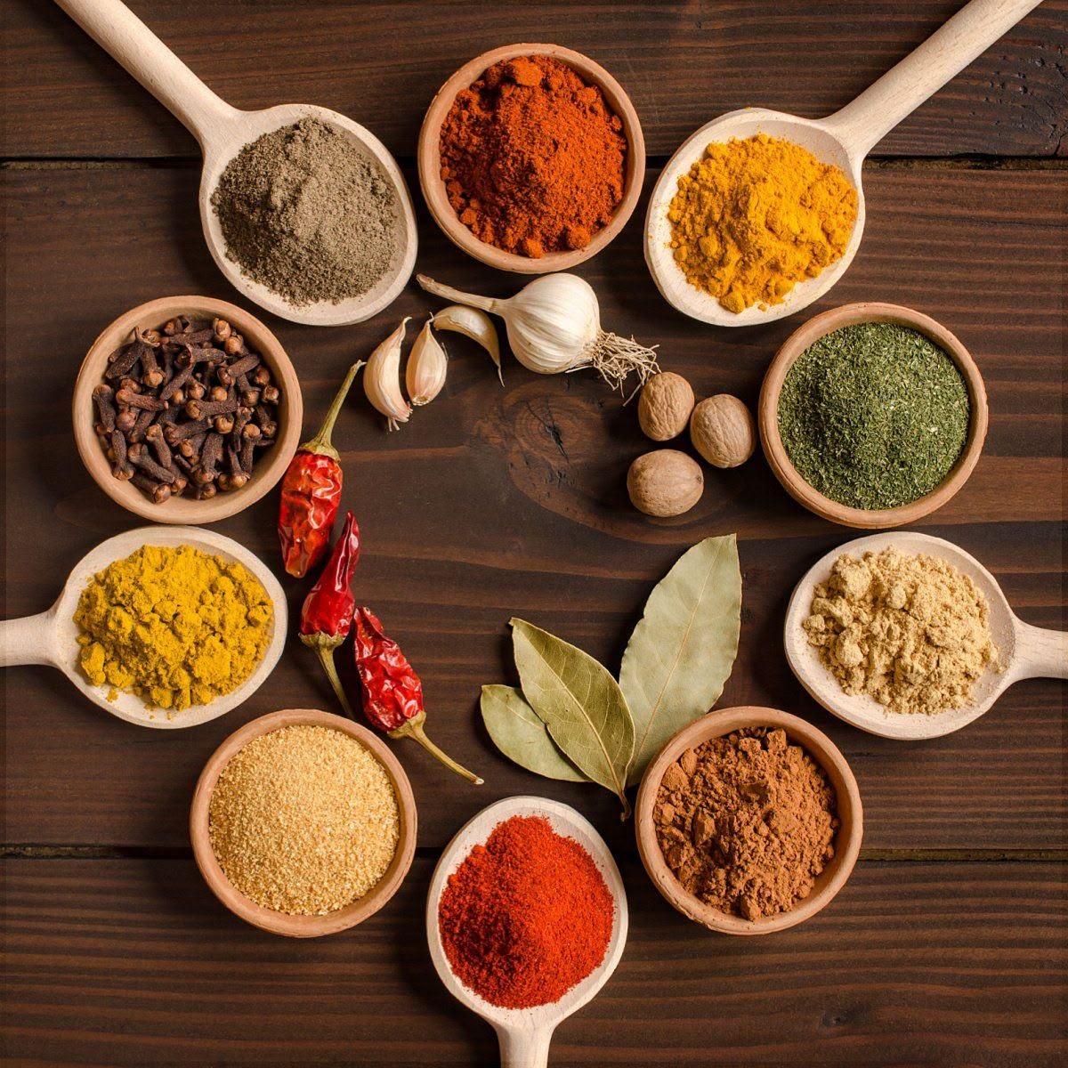 A circular arrangement of ground spices and botanicals in small bowls and spoons